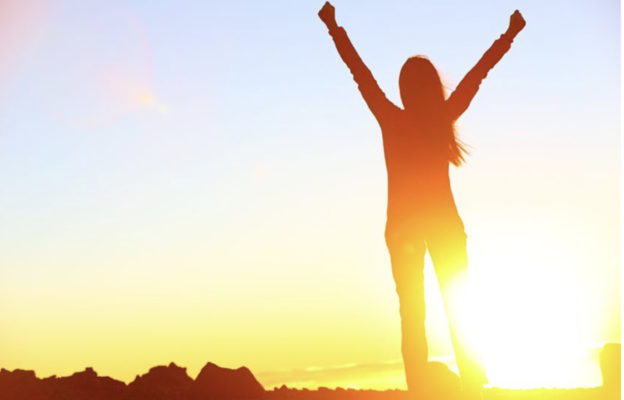 Person standing at sunrise with arms up in the air